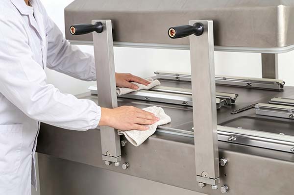 Wiping the interior of a chamber vacuum sealer with a damp cloth during cleaning